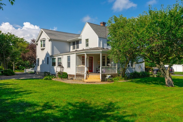 View of front facade with covered porch, a front lawn, and a shingled roof