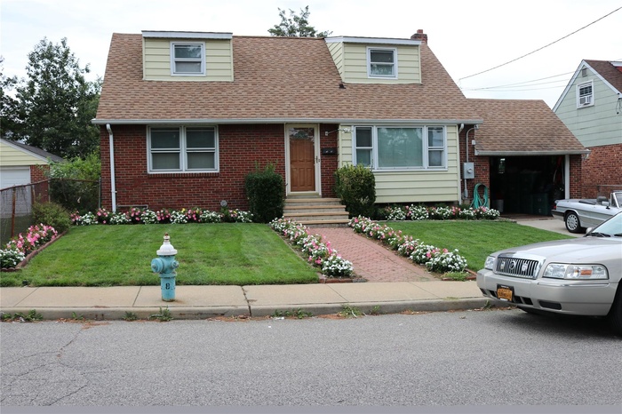 Cape cod home featuring roof with shingles, brick siding, a front lawn, and an attached garage