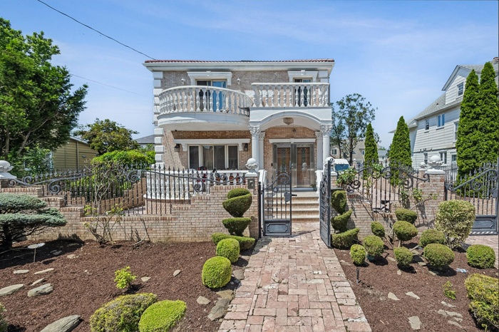 View of front facade featuring a balcony, brick siding, a fenced front yard, a gate, and french doors