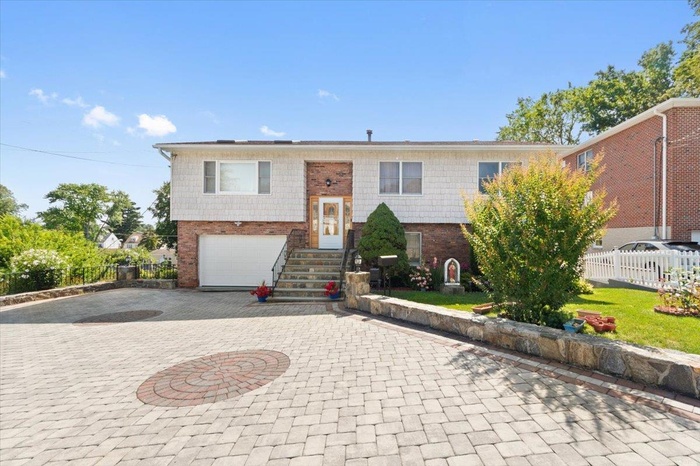 Bi-level home featuring decorative driveway, a garage, and brick siding
