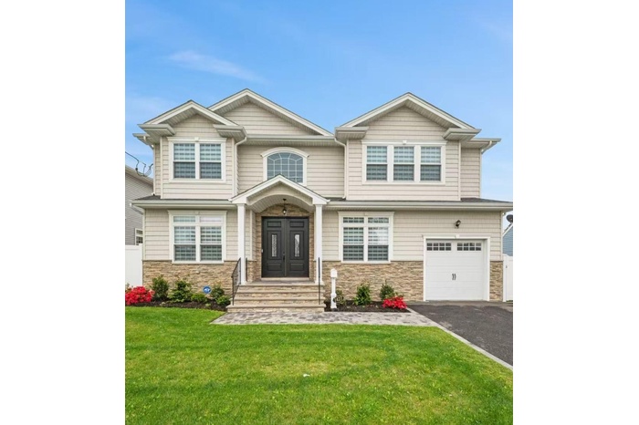 View of front facade with stone siding, asphalt driveway, a front lawn, and a garage