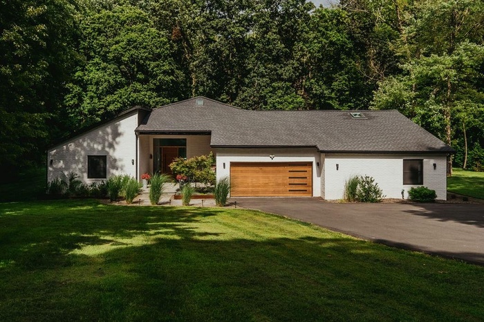 View of front facade with an attached garage, asphalt driveway, a front yard, and roof with shingles