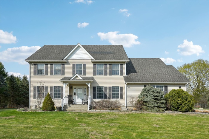 Colonial inspired home with a shingled roof and a front yard