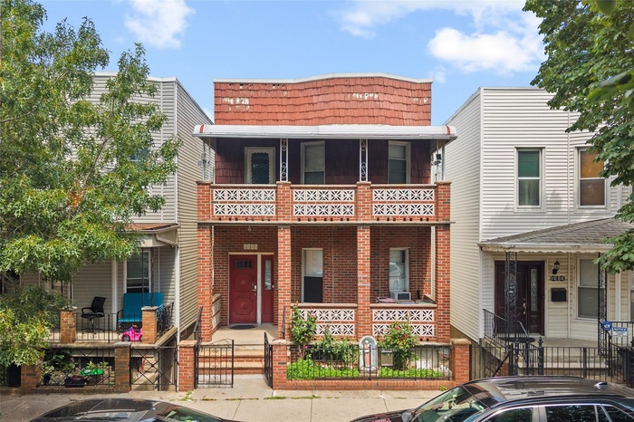 View of front of property featuring a fenced front yard, a porch, a gate, brick siding, and mansard roof