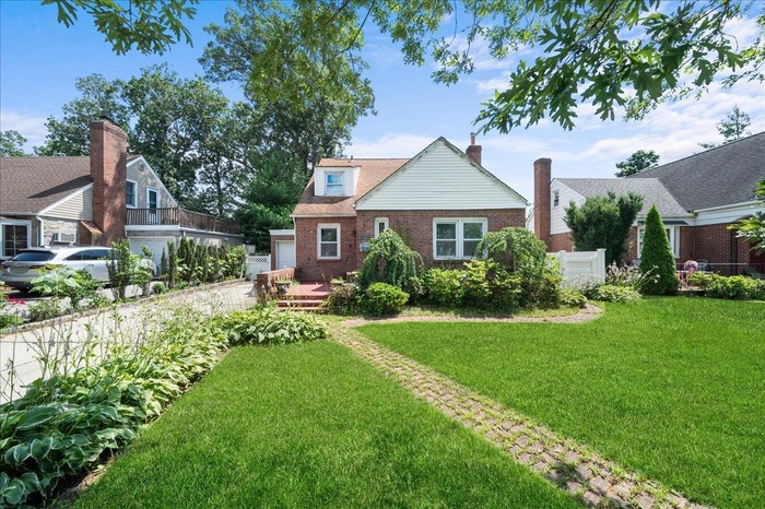 View of front facade featuring brick siding, a front yard, a garage, and a chimney