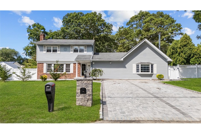 View of front of house with driveway, brick siding, a chimney, and roof with shingles