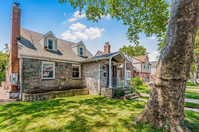 New england style home featuring a chimney, stone siding, a front lawn, and a shingled roof