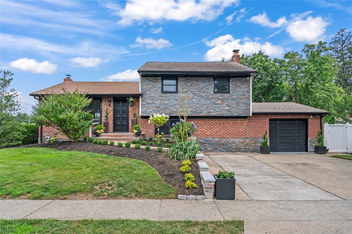 Tri-level home featuring a chimney, an attached garage, concrete driveway, and roof with shingles