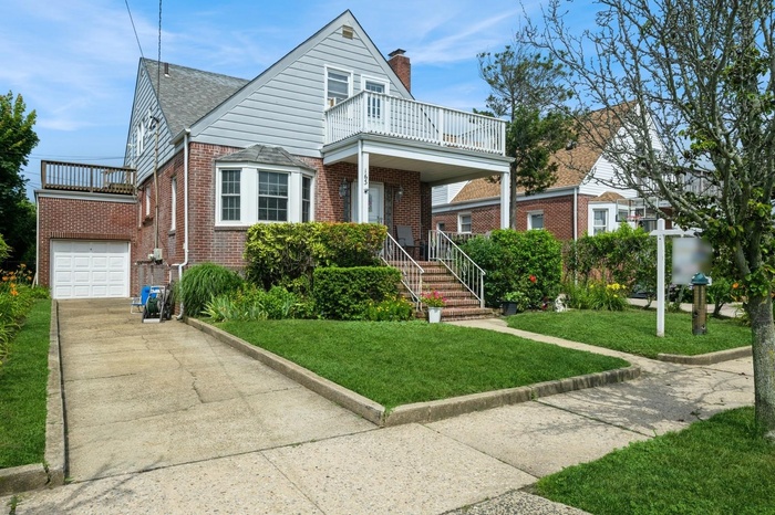 View of front of house with a balcony, driveway, brick siding, a front lawn, and a chimney