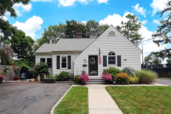 View of front facade with a chimney, roof with shingles, and driveway