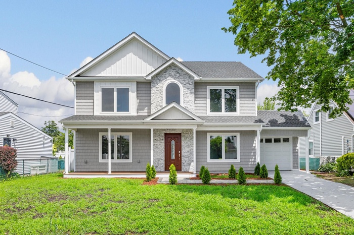 View of front of home featuring covered porch, roof with shingles, board and batten siding, driveway, and a front lawn
