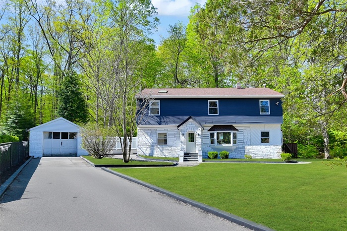Colonial inspired home featuring stone siding, asphalt driveway, an outdoor structure, and a garage