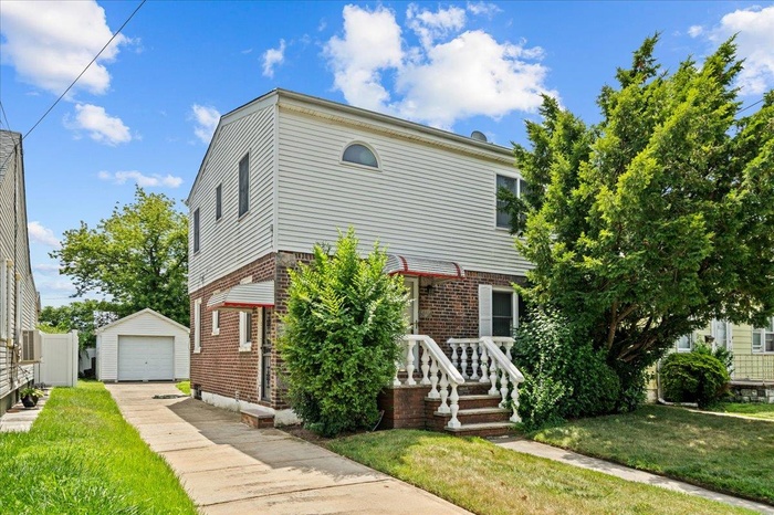 View of front of property featuring an outbuilding, concrete driveway, a garage, brick siding, and a front yard