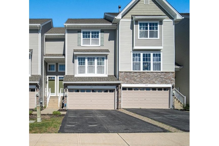 View of front facade with asphalt driveway, stone siding, a shingled roof, and a garage