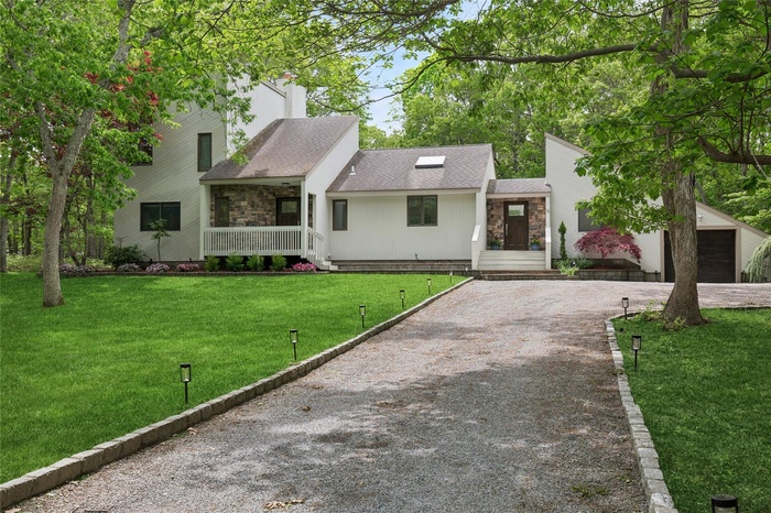 View of front of home with driveway, stone siding, roof with shingles, and a front lawn