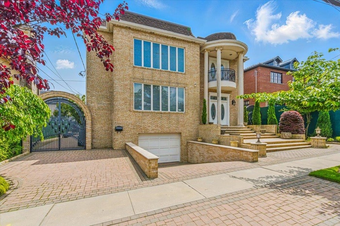 View of front of home featuring decorative driveway, a balcony, brick siding, an attached garage, and a gate