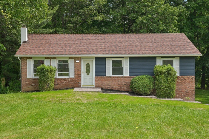 Ranch-style house with a chimney, brick siding, a front yard, and a shingled roof
