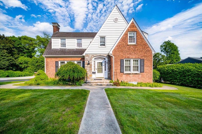 Tudor house featuring a chimney, brick siding, a front lawn, and roof with shingles