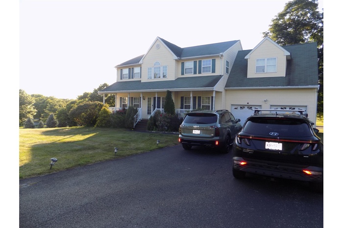Colonial-style house featuring asphalt driveway, covered porch, a front yard, and an attached garage