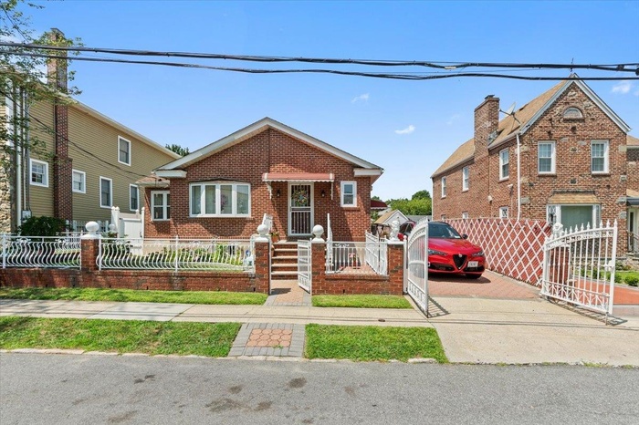 View of front of property featuring a fenced front yard, a gate, brick siding, and driveway