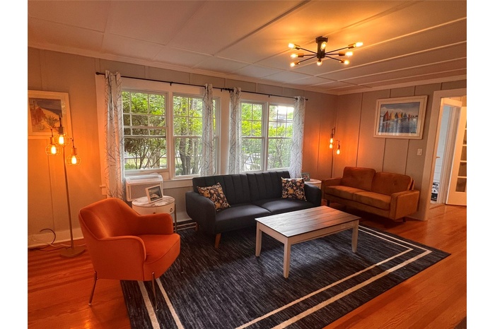 Living room with wood finished floors, healthy amount of natural light, a chandelier, and ornamental molding