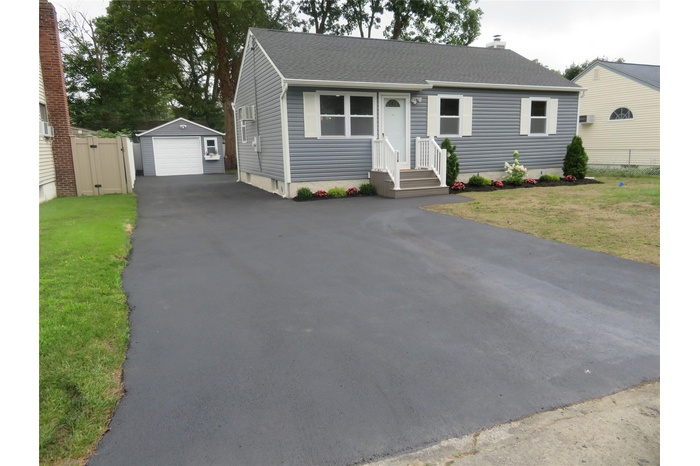 View of front of house featuring driveway, a garage, roof with shingles, an outdoor structure, and front yard.