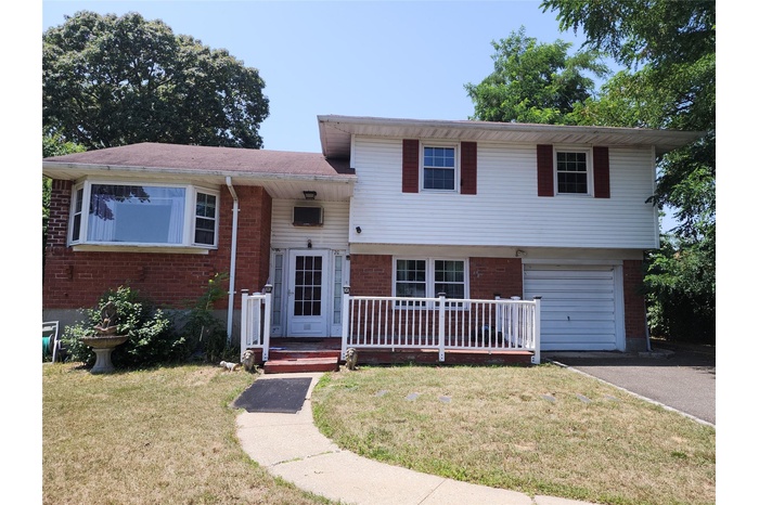 Tri-level home with brick siding, a front yard, an attached garage, and asphalt driveway