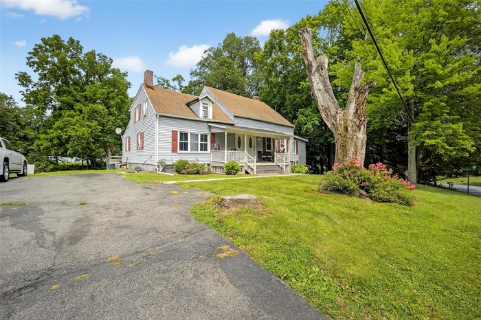 View of front of property with covered porch, a chimney, a front yard, and view of scattered trees