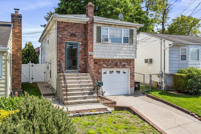 View of front of home with a gate, driveway, fence, a garage, and brick siding
