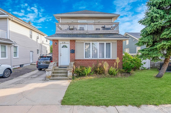 View of front of property featuring a front yard, a shingled roof, a balcony, brick siding, and driveway