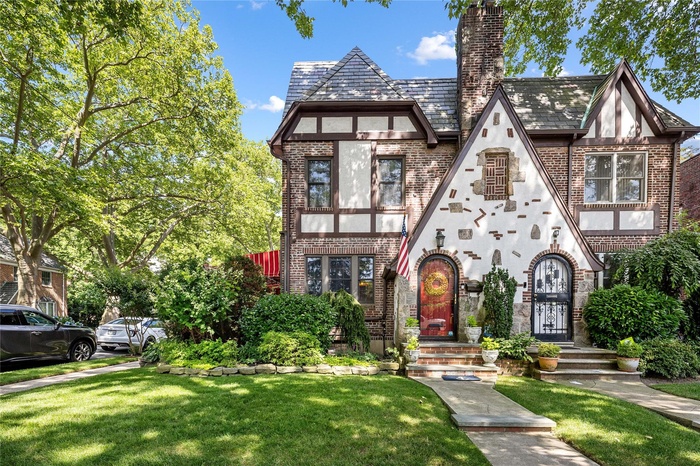 Tudor house with brick siding, a front yard, a chimney, and stucco siding
