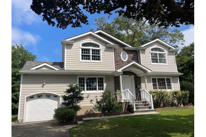 View of front of property with a front yard, driveway, an attached garage, and stone siding