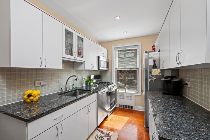Kitchen with white cabinets, stainless steel appliances, radiator heating unit, a sink, and light wood-type flooring