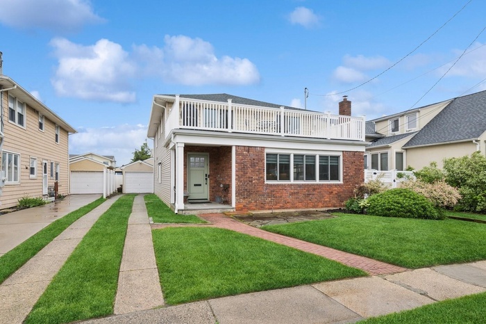 View of front of house featuring a balcony, brick siding, an outdoor structure, a front lawn, and a garage