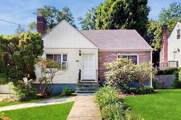 View of front of property with entry steps, a front lawn, a chimney, stone siding, and a shingled roof