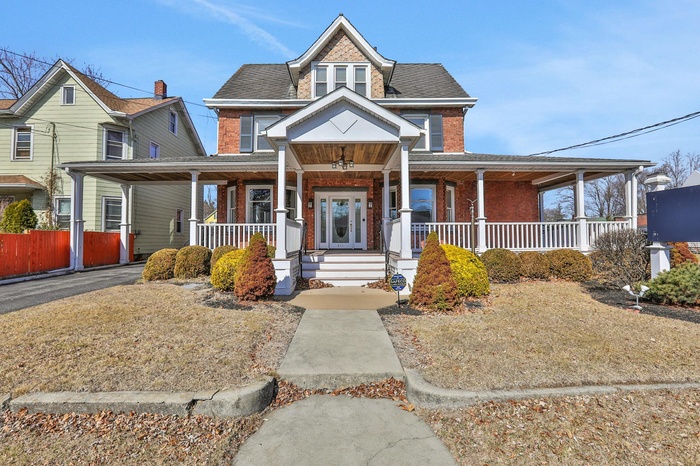 View of front of property featuring covered porch, brick siding, and roof with shingles