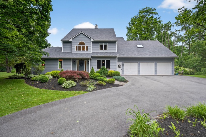 Traditional-style house with an attached garage, driveway, a chimney, a shingled roof, and a front yard