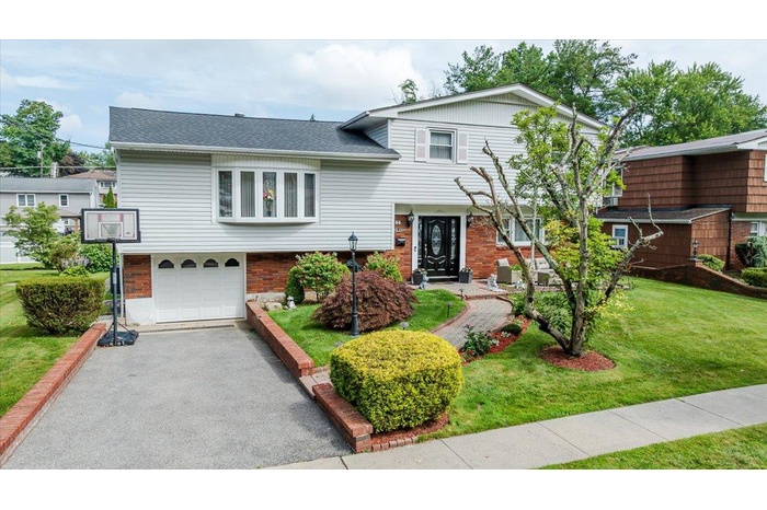 Tri-level home featuring a garage, a front yard, asphalt driveway, brick siding, and roof with shingles