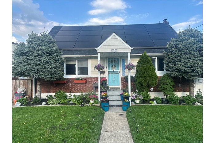 Bungalow-style home featuring a front lawn, brick siding, a chimney, roof with shingles, and solar panels