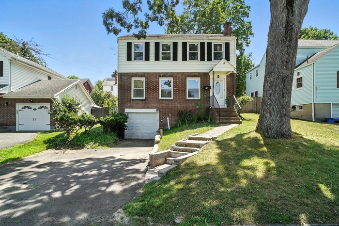 View of front of property featuring a chimney, asphalt driveway, brick siding, a front lawn, and an attached garage