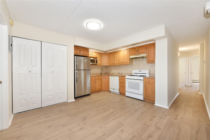 Kitchen featuring light countertops, light wood-style floors, under cabinet range hood, stainless steel appliances, and decorative backsplash