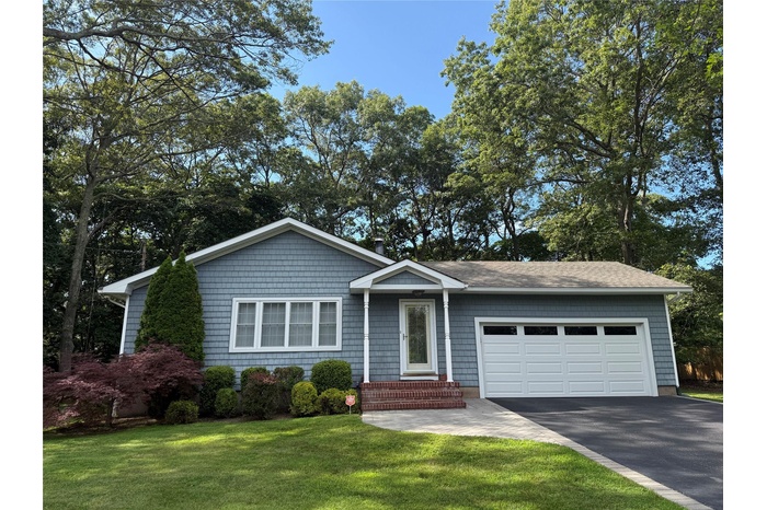 Single story home with a garage, driveway, a front lawn, and view of wooded area