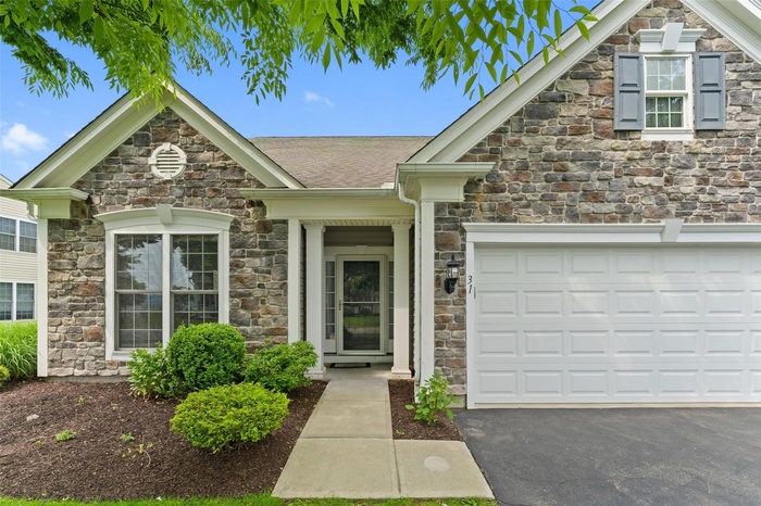 View of front of house featuring stone siding, driveway, and a shingled roof