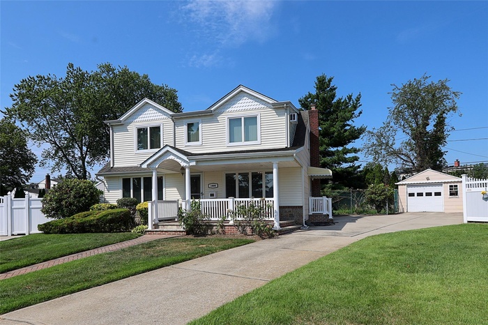 View of front of home featuring a porch, an outdoor structure, driveway, a detached garage, and a chimney