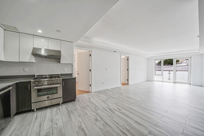 Kitchen with exhaust hood, stainless steel stove, open floor plan, modern cabinets, and white cabinetry