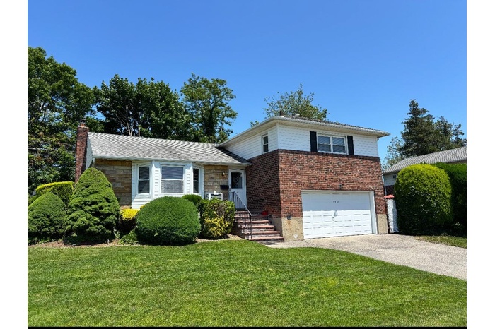 Tri-level home featuring a garage, concrete driveway, a front yard, a chimney, and stone siding