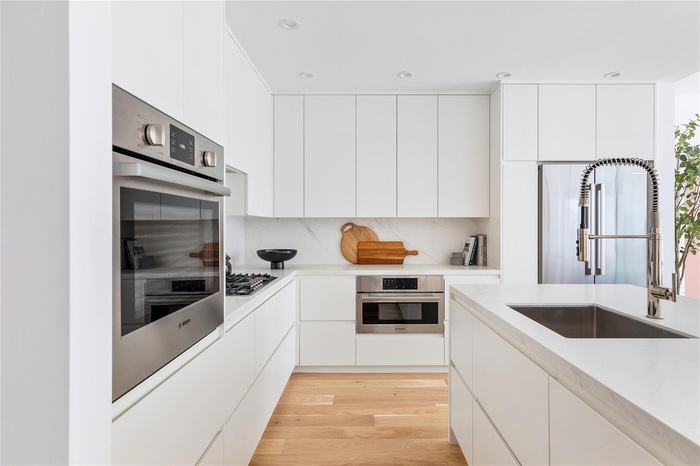 Kitchen featuring modern cabinets, a sink, stainless steel appliances, white cabinets, and light countertops