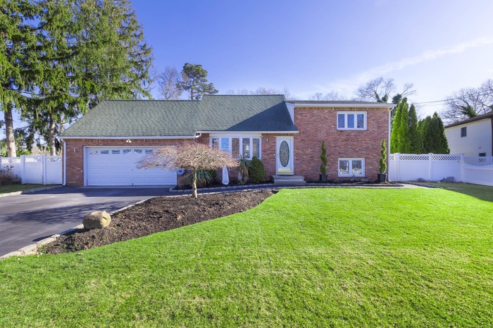 Tri-level home featuring brick siding, fence, concrete driveway, and a front yard