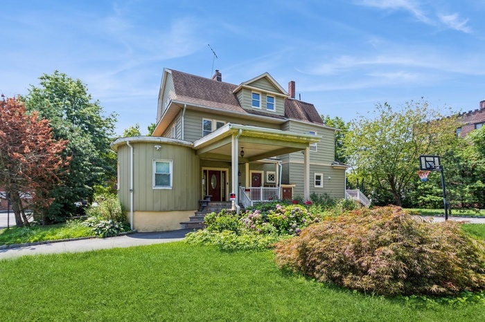 View of front facade with a chimney, a porch, a front yard, a shingled roof, and board and batten siding