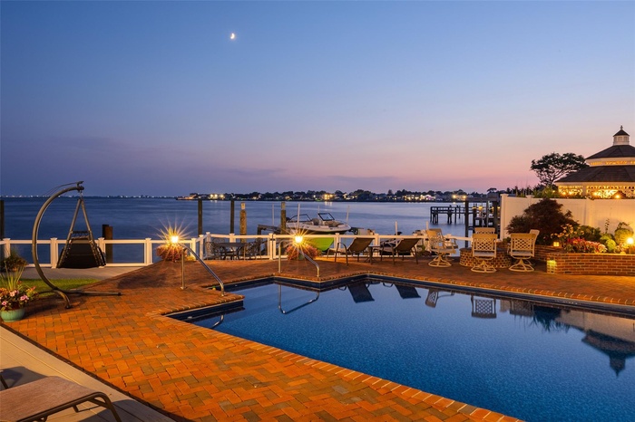 Pool at dusk featuring a water view and a patio area